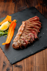 top view of delicious ribeye beef steak on the ribbon sliced on the black stone plate with carrots slices