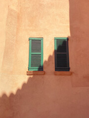 Abstract sun and shadow pattern cast on a traditional rustic terracotta colour old wall with green shutters in St Tropez, The South of France