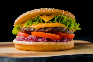 hamburger with beef cutlet, tomato, salad leaves, cedar cheese, red marinated onion with french fries on the wooden plate on the dark background   