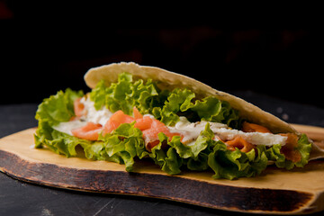 Healthy Italian sandwich with salad leaves, smoked raw salmon, white sauce on the wooden board on the black background