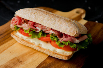 healthy delicious sandwich with salad leaves, prosciutto crudo, tomato, white sauce on the wooden board, dark background  