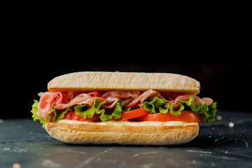 healthy delicious sandwich with salad leaves, prosciutto crudo, tomato, white sauce on the wooden board, dark background  