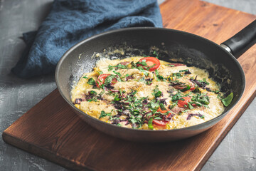 Cooked omelette with sausage, cheese, tomato and herbs in a pan, on wooden board