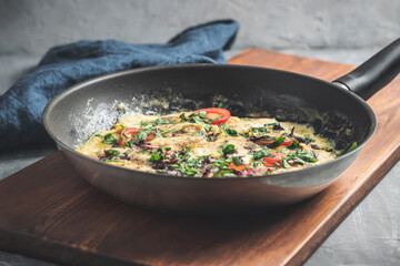 Cooked omelette with sausage, cheese, tomato and herbs in a pan, on wooden board
