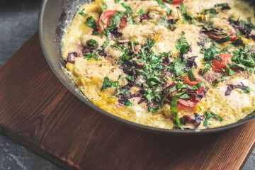Cooked omelette with sausage, cheese, tomato and herbs in a pan, on wooden board