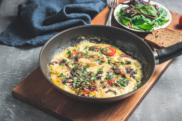 Cooked omelette with sausage, cheese, tomato and herbs in a pan, on wooden board