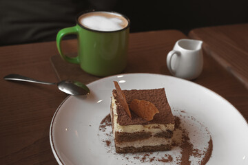 A piece of tiramisu cake in a restaurant. Cheese dessert. Tiramisu with coffee. Delicious cake. Italian cuisine. Sweet food. Cafe menu. Cozy coffee shop.