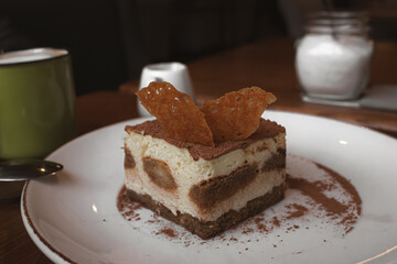 A piece of tiramisu cake in a restaurant. Cheese dessert. Tiramisu with coffee. Delicious cake. Italian cuisine. Sweet food. Cafe menu. Cozy coffee shop.