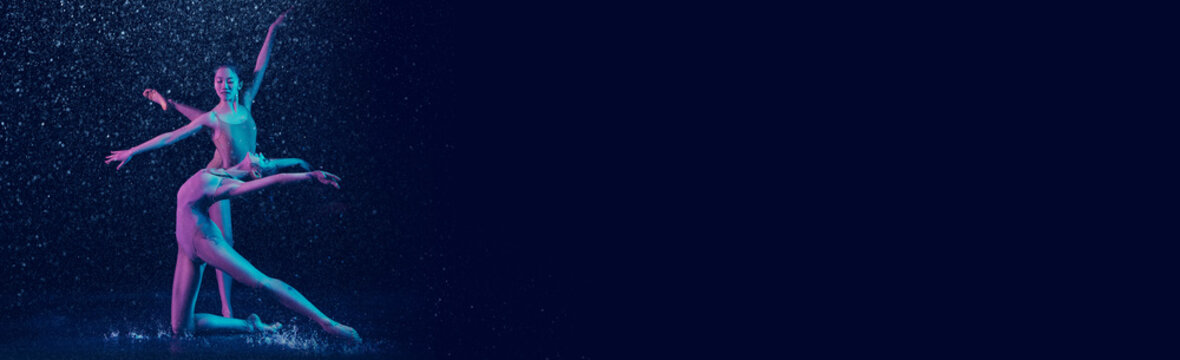 Grace, beauty, tenderness. Two young women. professional ballet dancer performing under water drops over dark blue background in neon light. Ballet and contemporary choreography concept. Banner