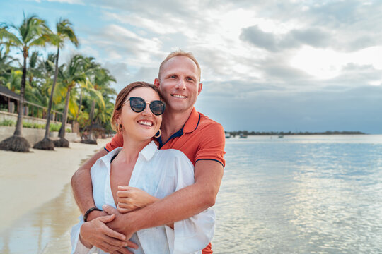 Smiling couple in love hugging on the sandy exotic beach while have evening walk by the Trou-aux-Biches seashore on Mauritius island. People relationship and tropic honeymoon vacations concept image.