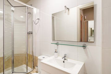 Bathroom with light beige walls. In corner is a shower with glass sliding doors. Vanity sink with white furniture and toilet.