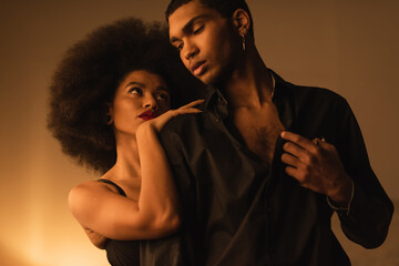 sensual african american woman embracing young man in black shirt while seducing him at night