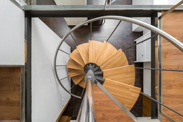 Modern spiral staircase with wooden steps and metal railings looking down from above creates a...