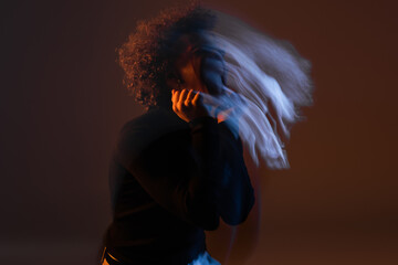 motion blur of young african american man with bipolar disorder on dark background with orange and...