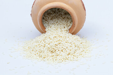 Grain sticky rice overflowing from clay pot on white background. Rice is cereal that is consumed by...
