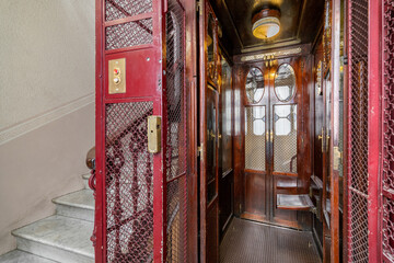 Empty retro style elevator with red metal bars, doors on both sides, inside with dark polished wood...