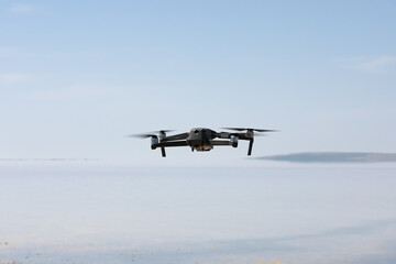 Fototapeta na wymiar Dark gray unmanned drone quadcopter flying isolated over a body of water, soft focus