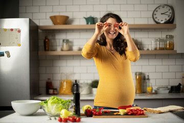 Beautiful pregnant woman preparing delicious food. Smiling woman having fun while cooking at home.