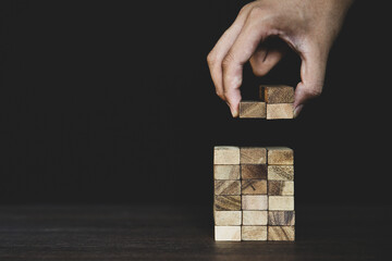 Hand placing wooden block tower stack in pyramid stair step with caution to prevent collapse or...