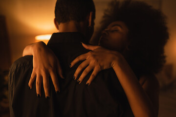 seductive african american woman embracing man in black shirt in dark room with lighting