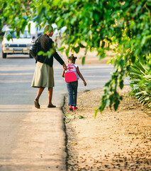 mother and small african girl with a backpack walking to school