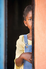 shy small african girl with braids  hiding in the door frame a