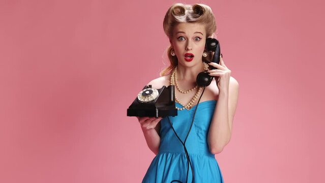 Emotional phone talk. Beautiful young girl with stylish hair and bright makeup talking with different emotions on pink background. Concept of retro fashion, beauty, attraction, 50s, 60s. Pin-up style