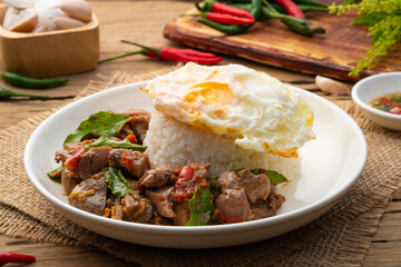 Stir-fried Chicken Giblets(livers, heart and gizzards) with Chillies and basil in white plate with cooked rice and put on top of a fried egg