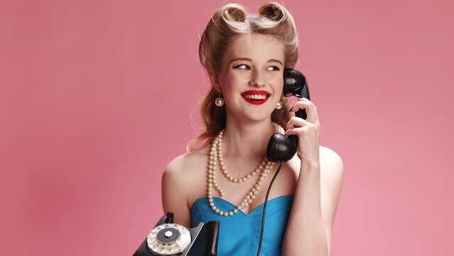 Beautiful young girl with blonde hair taking on phone over pink studio background. Diversity of emotions. Concept of retro fashion, beauty, attraction, 50s, 60s. Pin-up style. Vintage
