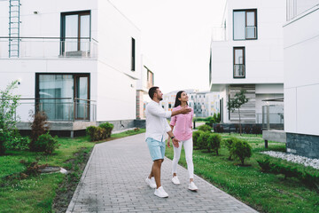 Joyful diverse couple walking on pathway between residential buildings outdoors