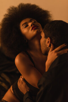 african american man kissing passionate and curly woman in bedroom at night