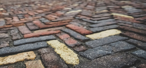 Antique paving stones of different shades are laid out in a herringbone pattern like parquet in macro with a blurred background in the city of Chernihiv, on a cloudy spring day after rain