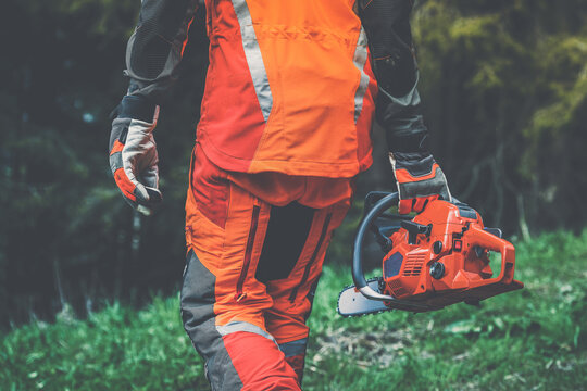 Close up view of an hand holding a chainsaw. Lumberjack at work wears orange personal protective equipment. Gardener working outdoor in the forest. Security, professionalism, occupation worker concept