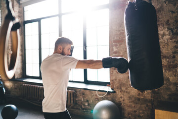Focused male boxer standing with punching bag