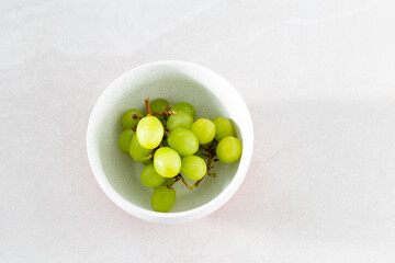 Selective focus flat lay side lit view of green grapes in white lightly speckled bowl on ceramic background