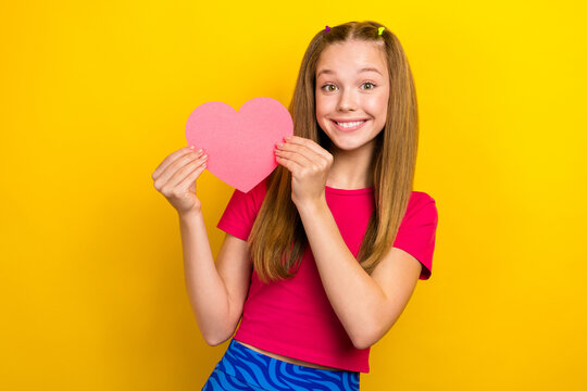 Photo of youngster teen age girl wear pink t-shirt crop top hold paper pink love symbol feelings first boyfriend isolated on yellow color background