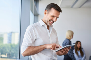 Handsome adult businessman standing in office using digital tablet