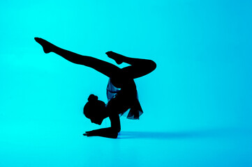 Fototapeta na wymiar Silhouette of a gymnast who performs exercises with a ball. Blue background