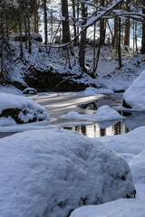 Teilweise gefrorener Fluss in Winterwald mit Schnee und Sonne