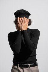 young african american man in stylish beret and black turtleneck covering face with hands isolated on grey