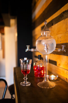 Close up of a traditional ornate absinthe  fountain with a glass and bottle of red liqueur