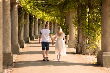 Fototapeta na wymiar Couple holding hands and walking under the pergola overgrown with green vegetation. Summer love.