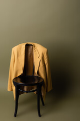 fashionable yellow blazer hanging on black wooden chair on olive green background