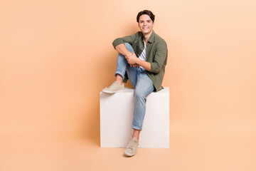 Full length photo cadre of young positive brunet hair man sitting comfortable cube platform wear...