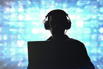 Silhouette of a military man in headphones at a laptop against the background of a video wall of glowing screens, contour lighting. Concept: information gathering, surveillance and control. - obrazy, fototapety, plakaty