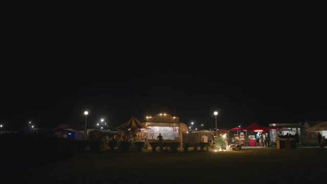 Rows of illuminated tents with drinks and food at a city festival in the park. Slow motion