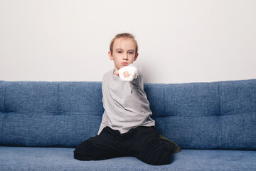Kid with broken arm and gypsum sitting on the sofa. Injury, traumas, accident by kids.
