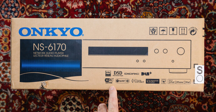 Paris, France - Dec 13, 2022: POV male hand pointing to cardboard package of new Onkyo NS-6170 network audio player with DSD Hi-Res Audio and DSD DAB+ WIFI device carpet rug silk background