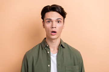 Obraz premium Photo of handsome astonished impressed guy with brunet hair dressed khaki shirt staring open mouth isolated on beige color background