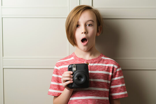 Cute boy taking selfe with photo camera. Stylish kid over grey background.